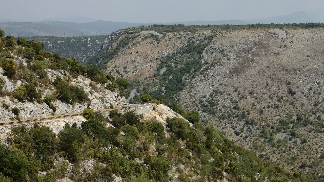 The wide green Neretva valley in Herzegovina seen from above, the river winding between limestone hills